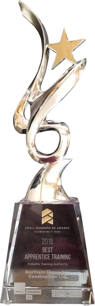 A gold trophy upon a crystal base. The base is engraved with text and logos. Small Business BC Awards Celebrating 15 Years 2018 Best Apprentice Training Industry Training Authority Northern Legendary Construction Ltd. (Small Business BC Logo) (Canada Post / Postes Canada Logo)