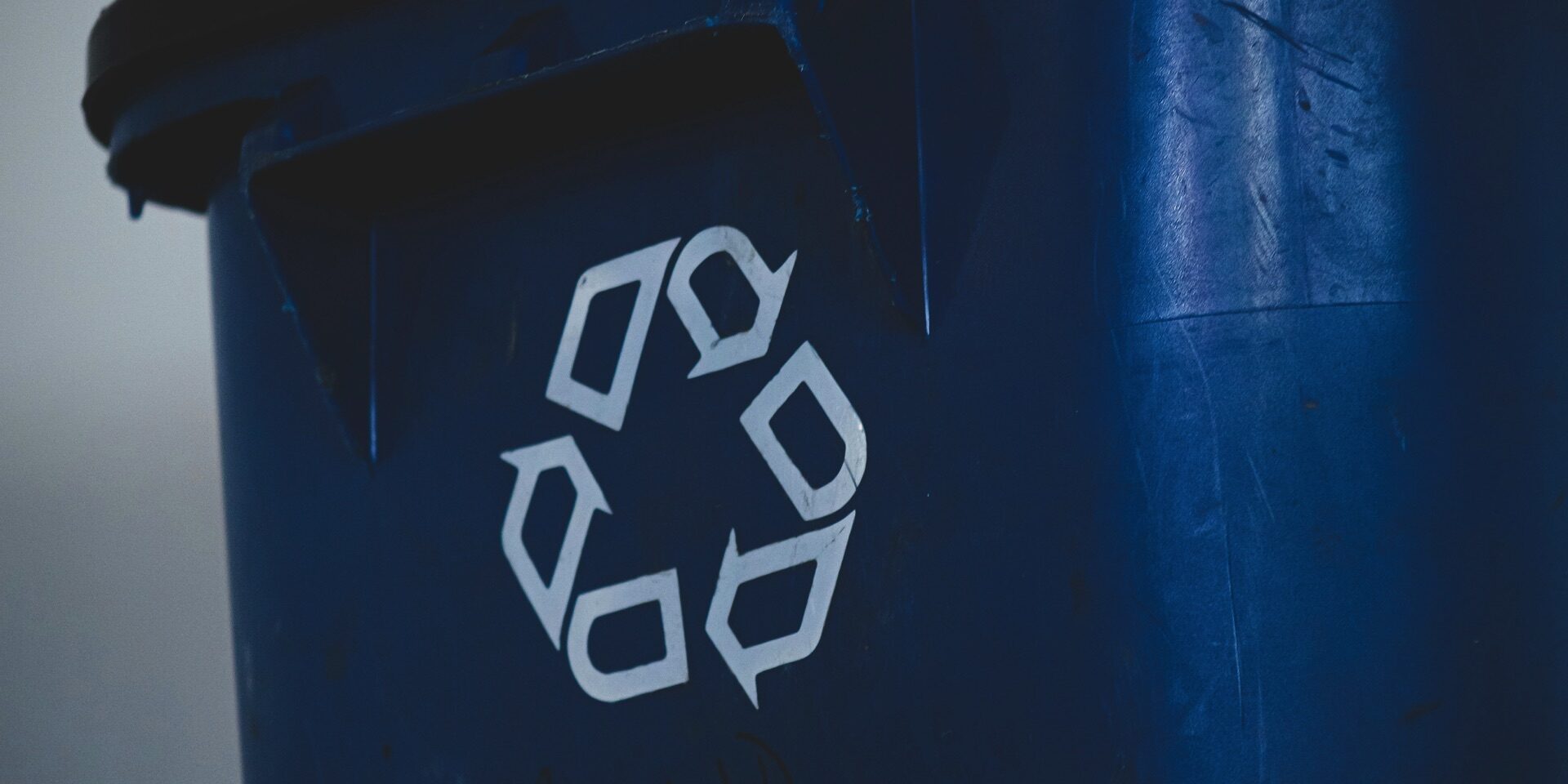 A blue recycling bin with the recycling symbol in white, scuffed up from regular use